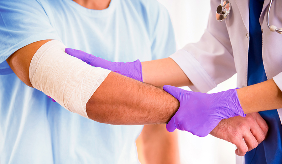 Patient with bandage on arm held by doctor wearing purple gloves