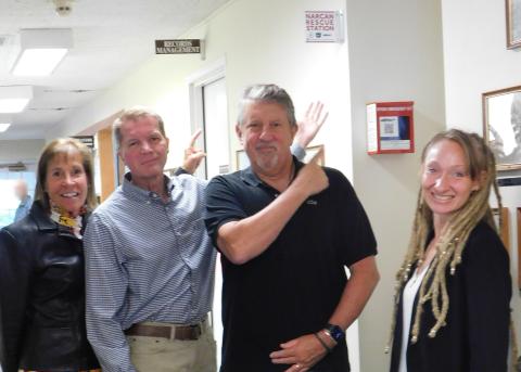 Two women and two men pointing at a Narcan Rescue Station.