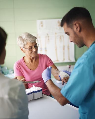Patient being bandaged by a doctor in blue scrubs wearing purple gloves in a hospital setting